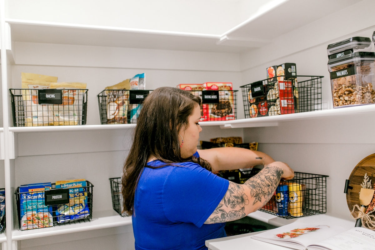 Woman arranging groceries into baskets on pantry shelves.