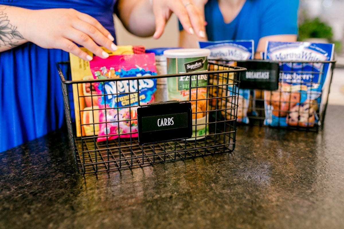 Hands organizing snacks into wire baskets on a countertop