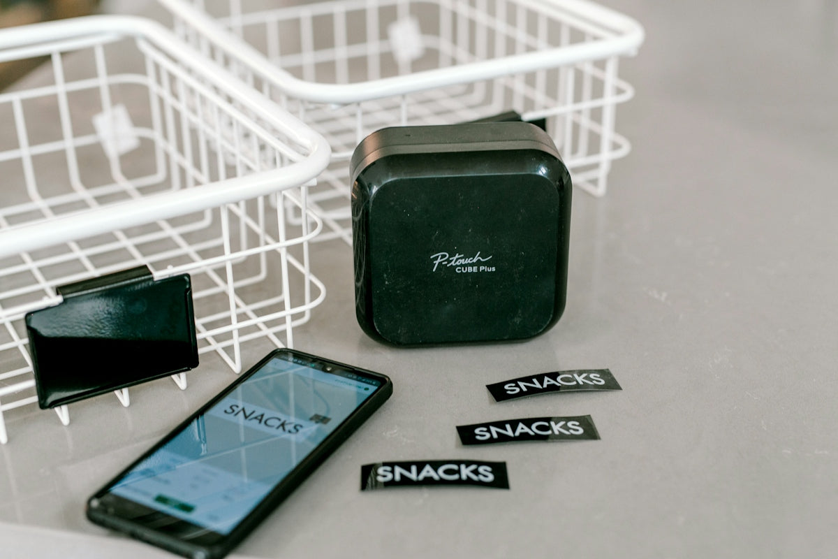 Label maker, smartphone, and snacks labels on a grey surface.