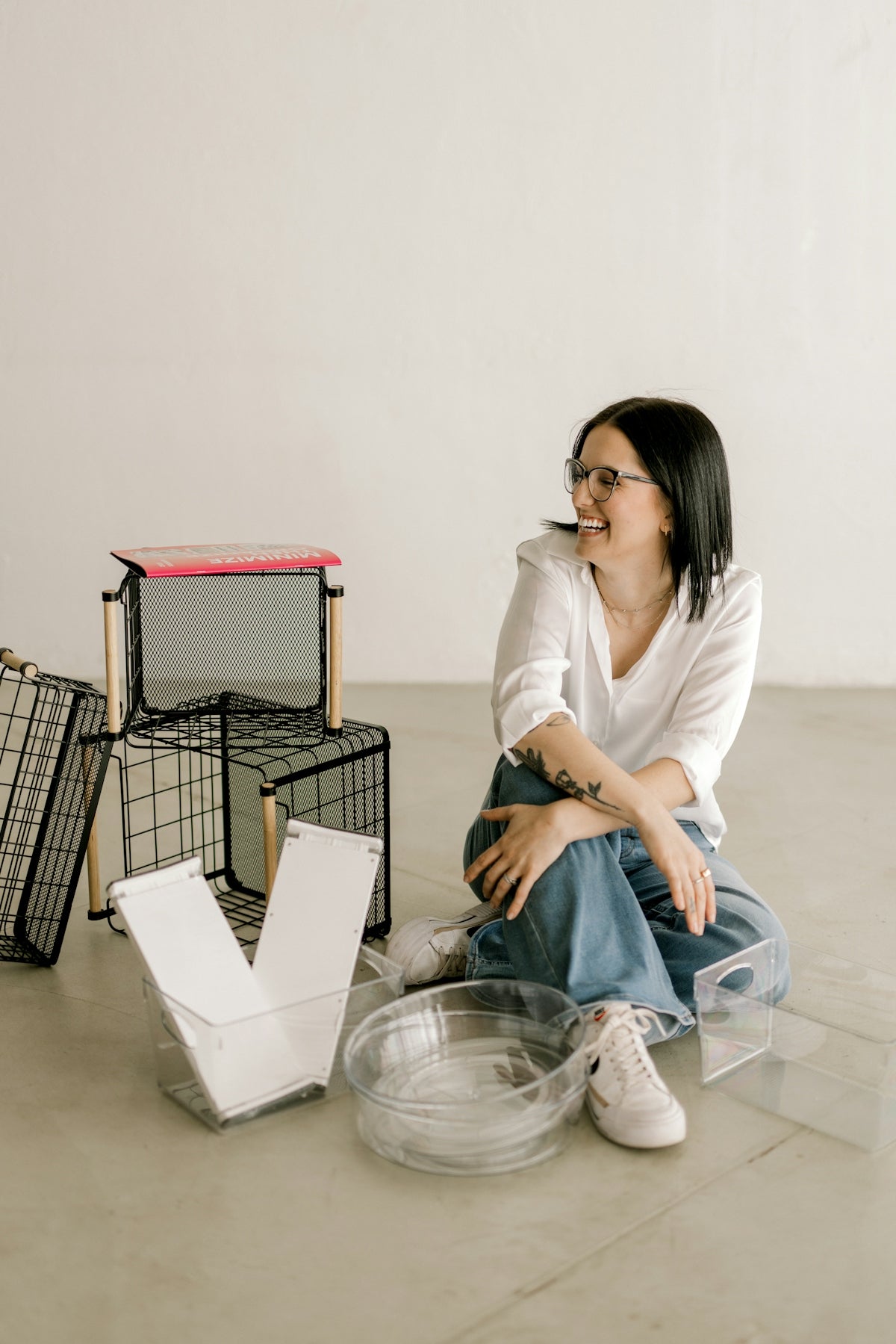 Smiling woman sits on floor with various clear storage containers.
