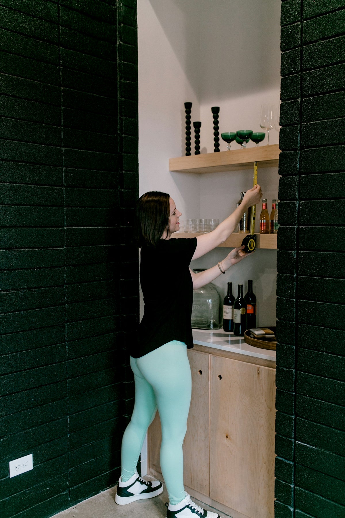 A woman measures shelves in a modern bar area.