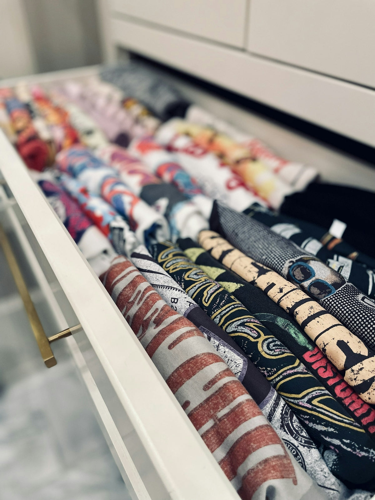 A drawer filled with neatly rolled graphic t-shirts in various colors and patterns